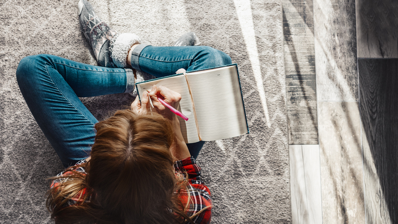 Young woman sitting on the floor at living room and writing into her diary for bible reading reflection