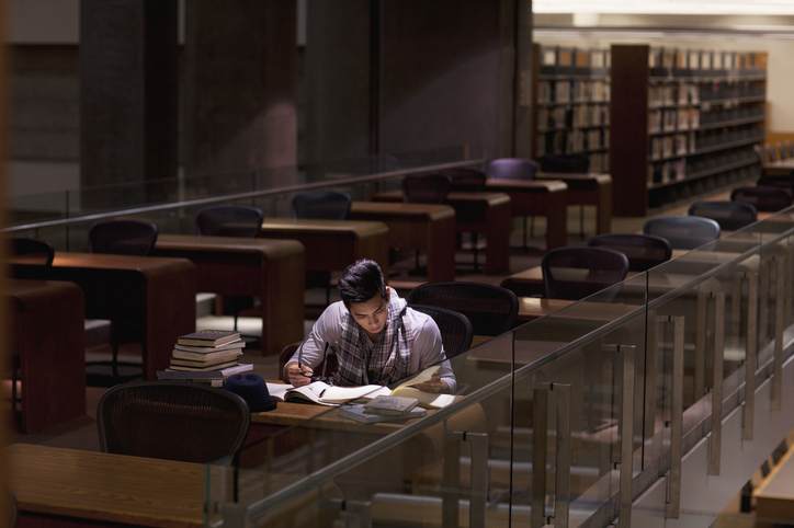 man alone in dark library reading a book with the words how to stick with your bible reading resolution on it