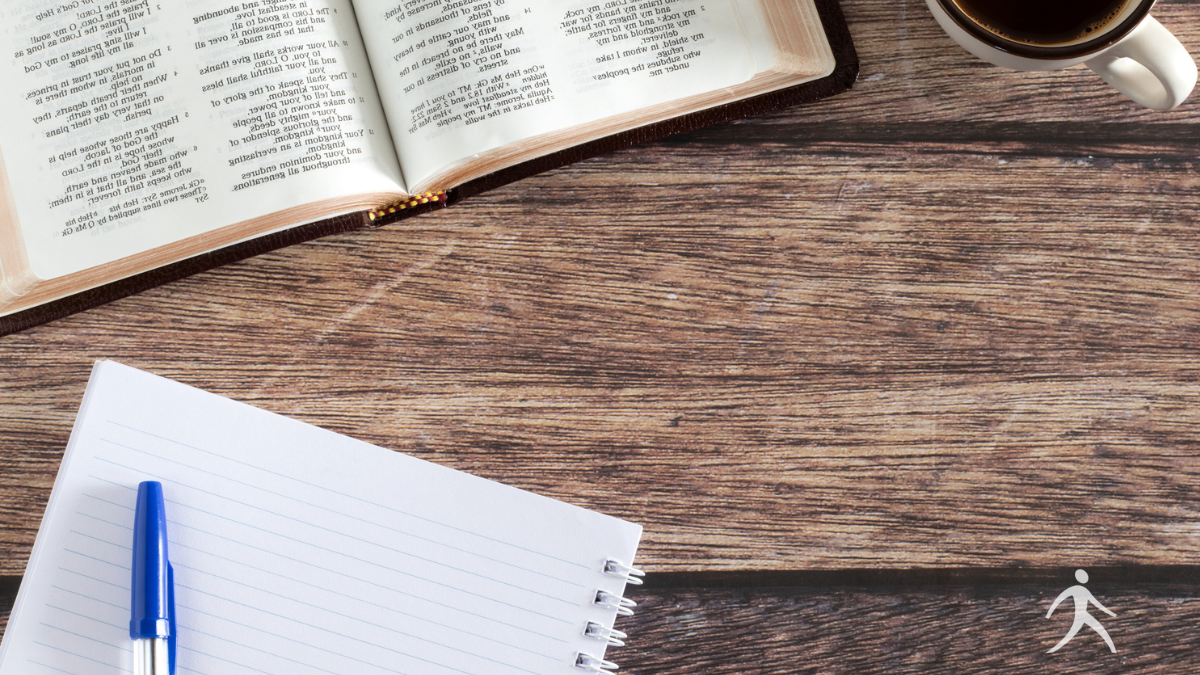 An open Bible with a journal and pen on a wooden table